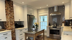 Een moderne keuken met witte kasten, een accentmuur van baksteen, roestvrijstalen apparatuur en een houten kookeiland met opbergruimte.