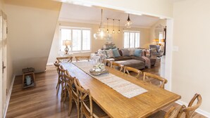 A spacious dining area with a long wooden table and chairs, a chandelier, and a cozy living room in the background. - Sea Beauty- MUST SEE 4 BD/ 3 BATH POOL! BCH ACCESS! (Virginia Beach)