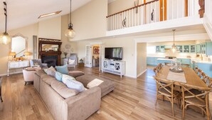 A spacious living room with a large sectional sofa, a dining area with a wooden table and chairs, and a kitchen with blue cabinets. - Sea Beauty- MUST SEE 4 BD/ 3 BATH POOL! BCH ACCESS! (Virginia Beach)