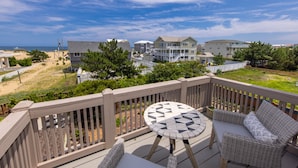 A wooden deck with a round table and wicker furniture, overlooking a beach and residential buildings. - Sea Beauty- MUST SEE 4 BD/ 3 BATH POOL! BCH ACCESS! (Virginia Beach)