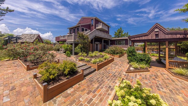 A two-story house with a balcony, surrounded by a garden with various plants and a brick pathway. - Sea Beauty- MUST SEE 4 BD/ 3 BATH POOL! BCH ACCESS! (Virginia Beach)