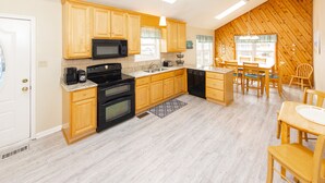 A kitchen with wooden cabinets, a microwave, a stove, and a dining area with wooden chairs and a table. - Lanikai- POOL/GAME RM/BAY & BCH ACCESS! (Virginia Beach)
