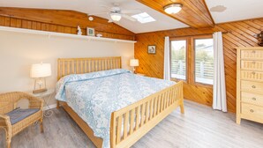 A bedroom with a wooden bed, a wicker chair, a dresser, and a window with curtains. - Lanikai- POOL/GAME RM/BAY & BCH ACCESS! (Virginia Beach)