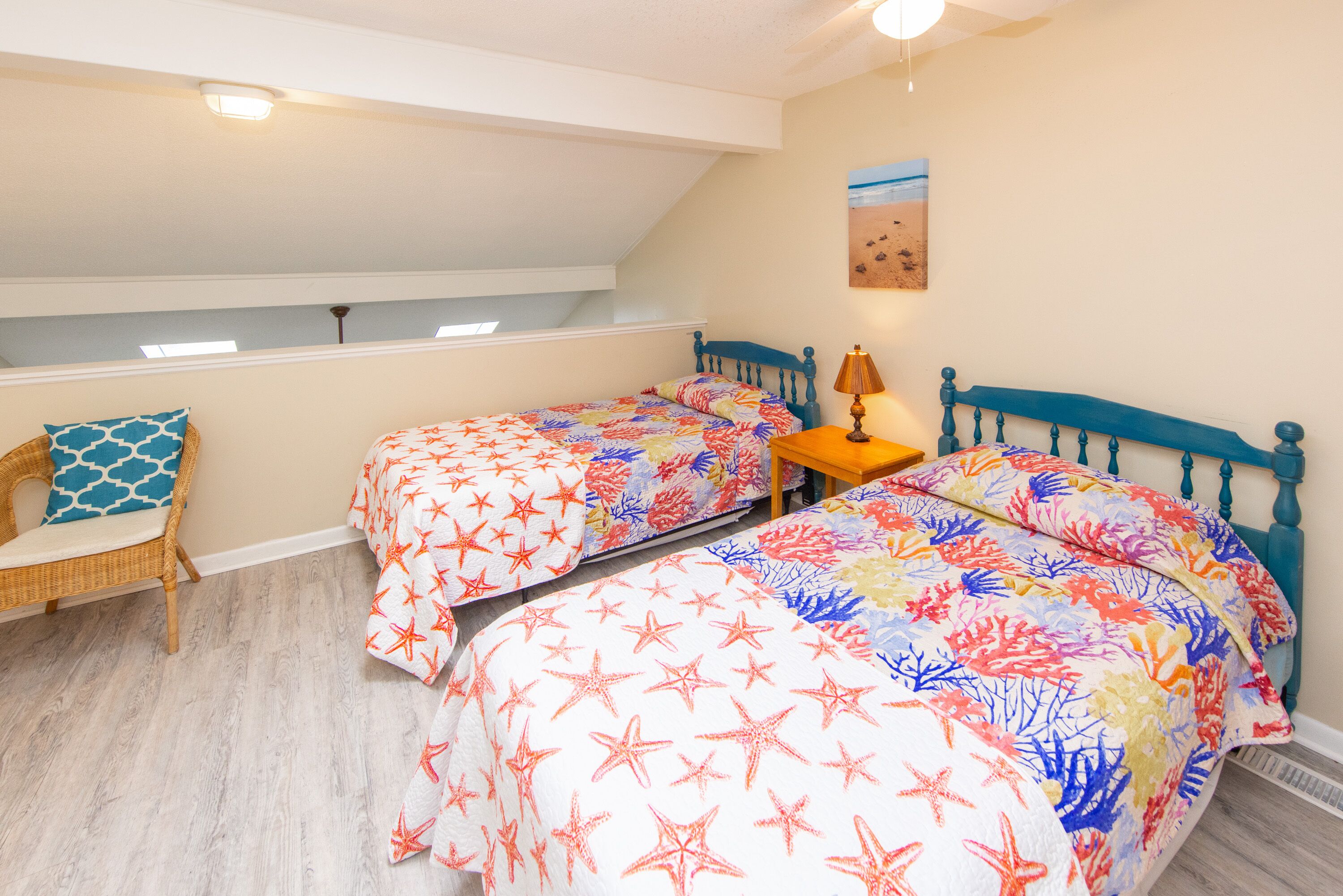 A bedroom with two beds, a small table, a chair, and a ceiling light.