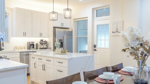 A modern kitchen with white cabinetry, a stainless steel refrigerator, and a dining area set for four with pink placemats and white dishes. - Queen Beds, EV Charging, Near Train: Luxury Stay (Chicago)