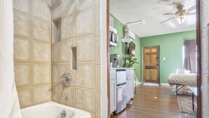 Une salle de bain avec une baignoire, une douche et des toilettes. On y trouve un lavabo avec un miroir et un meuble de rangement. Les murs de la pièce sont peints en vert et le sol est recouvert de parquet.
