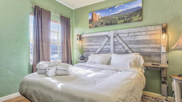 Un lit bien fait, avec du linge de lit blanc, une tête de lit en bois rustique et un tableau représentant un paysage accroché au mur.