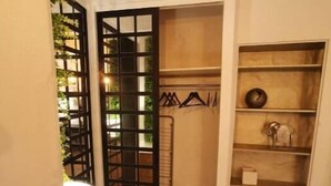 Ein kleiner Raum mit Holzboden, einem schwarzen Metallgitter, einer weißen Wand und einem Regal mit einigen Gegenständen.