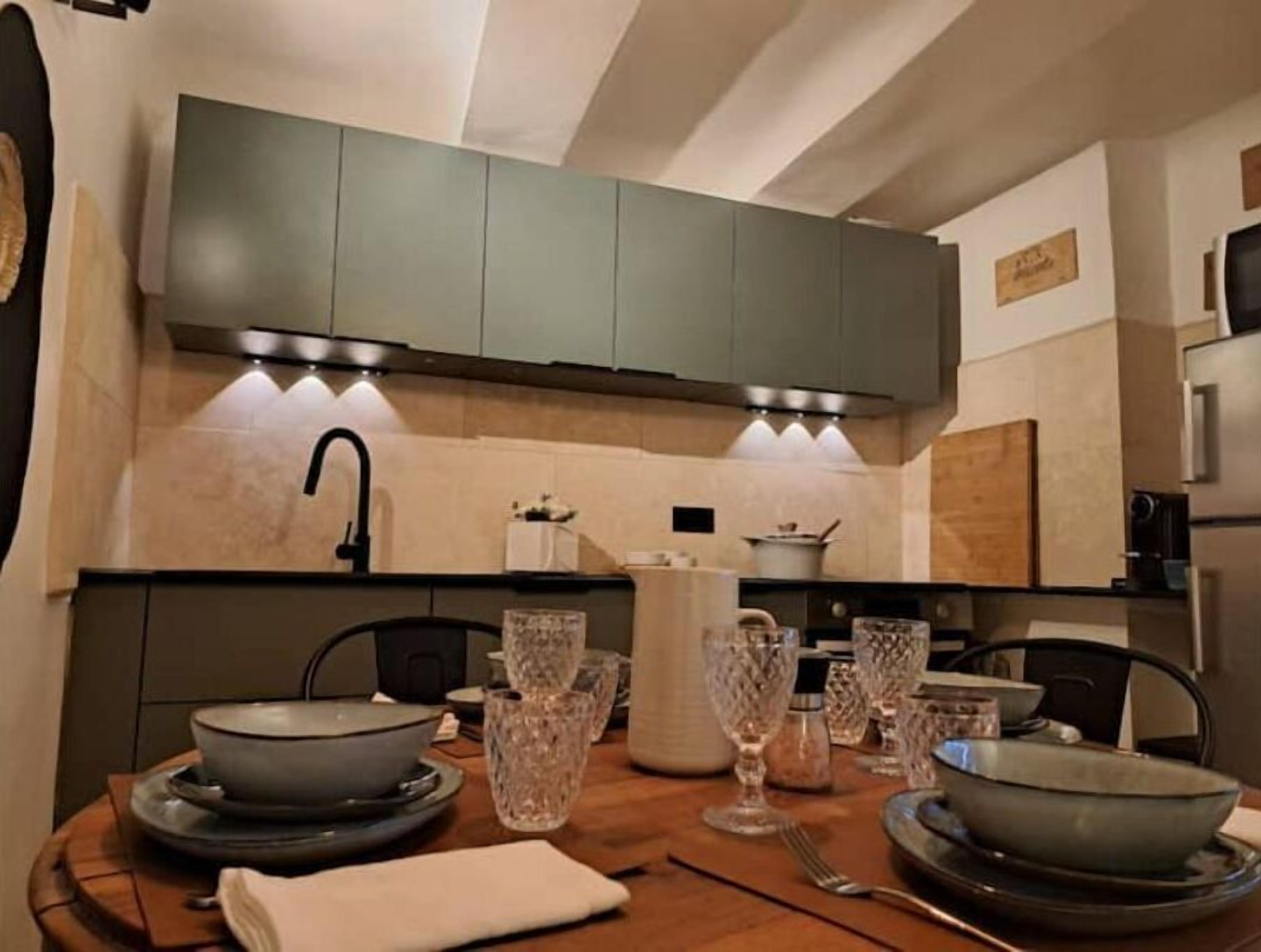Une cuisine moderne avec des meubles gris, un évier en acier inoxydable et une table à manger mise avec des bols, des verres et des couverts.