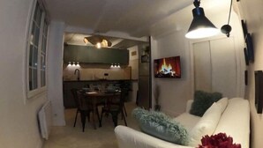 Ein gemütliches Wohnzimmer mit einem weißen Sofa, einem Esstisch und einer Küche im Hintergrund.