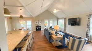 A spacious living area with a high ceiling, a dining area with wicker furniture, a sofa set, and a television mounted on the wall. - Gentleman Pirate (Ocean Views!) (Edisto Island)