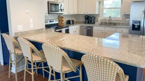 A modern kitchen with white cabinets, a large island, bar stools, and a built-in microwave. - Gentleman Pirate (Ocean Views!) (Edisto Island)