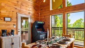 A wooden cabin with a dining table set for four, a coffee station, and a gaming console.