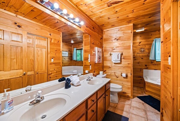 Baño de cabaña de madera con un tocador grande, dos lavamanos, un inodoro y una zona de ducha.
