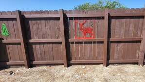 Una cerca de madera con varios adornos, incluyendo un cactus verde, un ciervo rojo y un mapa colorido de Texas.