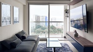 A modern living room with a sofa, a coffee table, a TV, and a balcony with a city view. - Ocean View 1BR - TV 65" - Pool - Jacuzzi 1606 (Barranco)