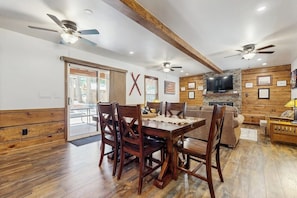A dining area with a wooden table and chairs, a television, and a stone fireplace.