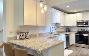 Uma cozinha moderna com armários brancos, bancadas de granito, eletrodomésticos de aço inoxidável e iluminação pendente.