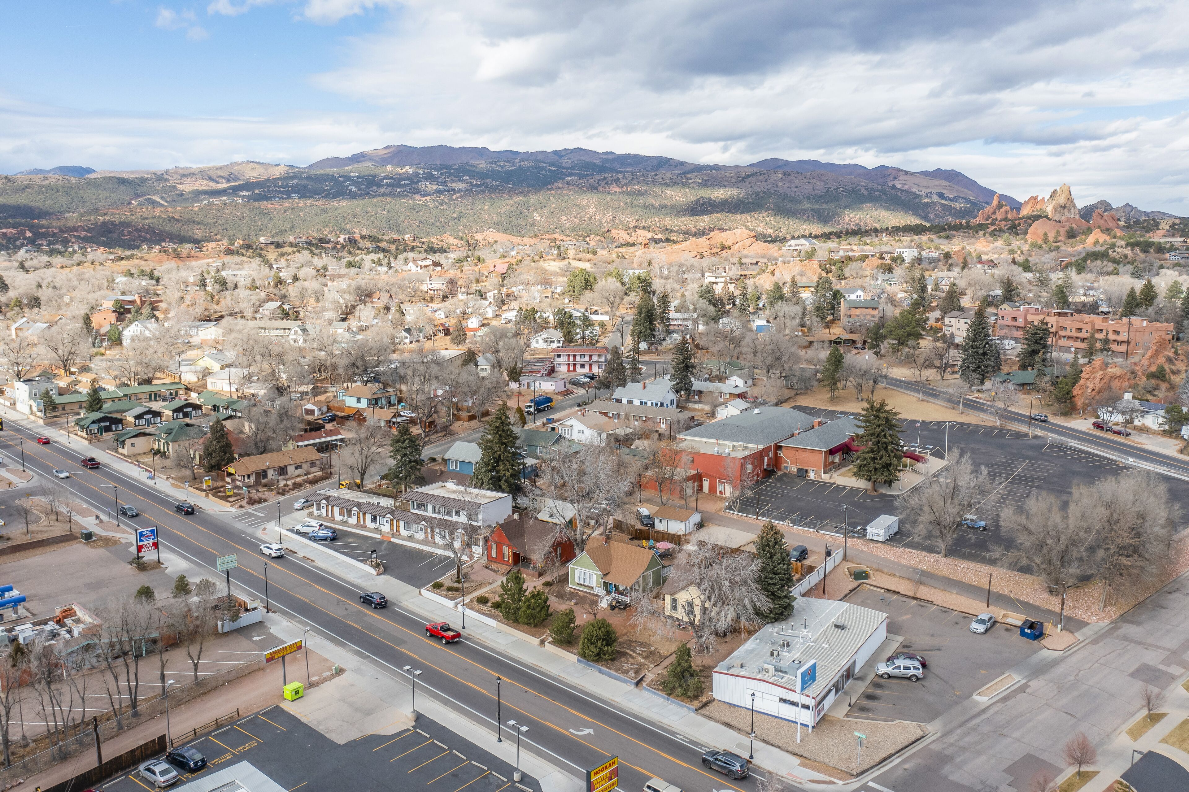 An aerial view of a town with a main road, buildings, and mountains in the background.