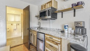 Une cuisine compacte équipée d’un four à micro-ondes encastré, d’une machine à café et de meubles de rangement en bois.