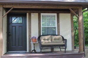 A porch with a dark door, a white window, and a wicker sofa.