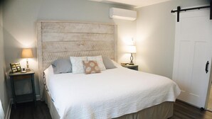A neatly made bed with a wooden headboard, two bedside tables with lamps, and a white door. - Storybook Cottage in the Woods (Geneva)