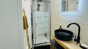 Uma casa de banho moderna com cabine de chuveiro em vidro, lavatório preto e toucador de madeira.
