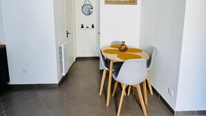 Uma área de refeições com uma mesa redonda e quatro cadeiras, um pequeno vaso sobre a mesa e um espelho fixado na parede.