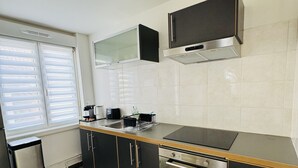 Uma cozinha moderna com armários pretos, forno de aço inoxidável, bancada preta e uma janela com persianas.