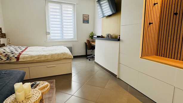 Quarto moderno com cama, mesa de cabeceira e televisão na parede.
