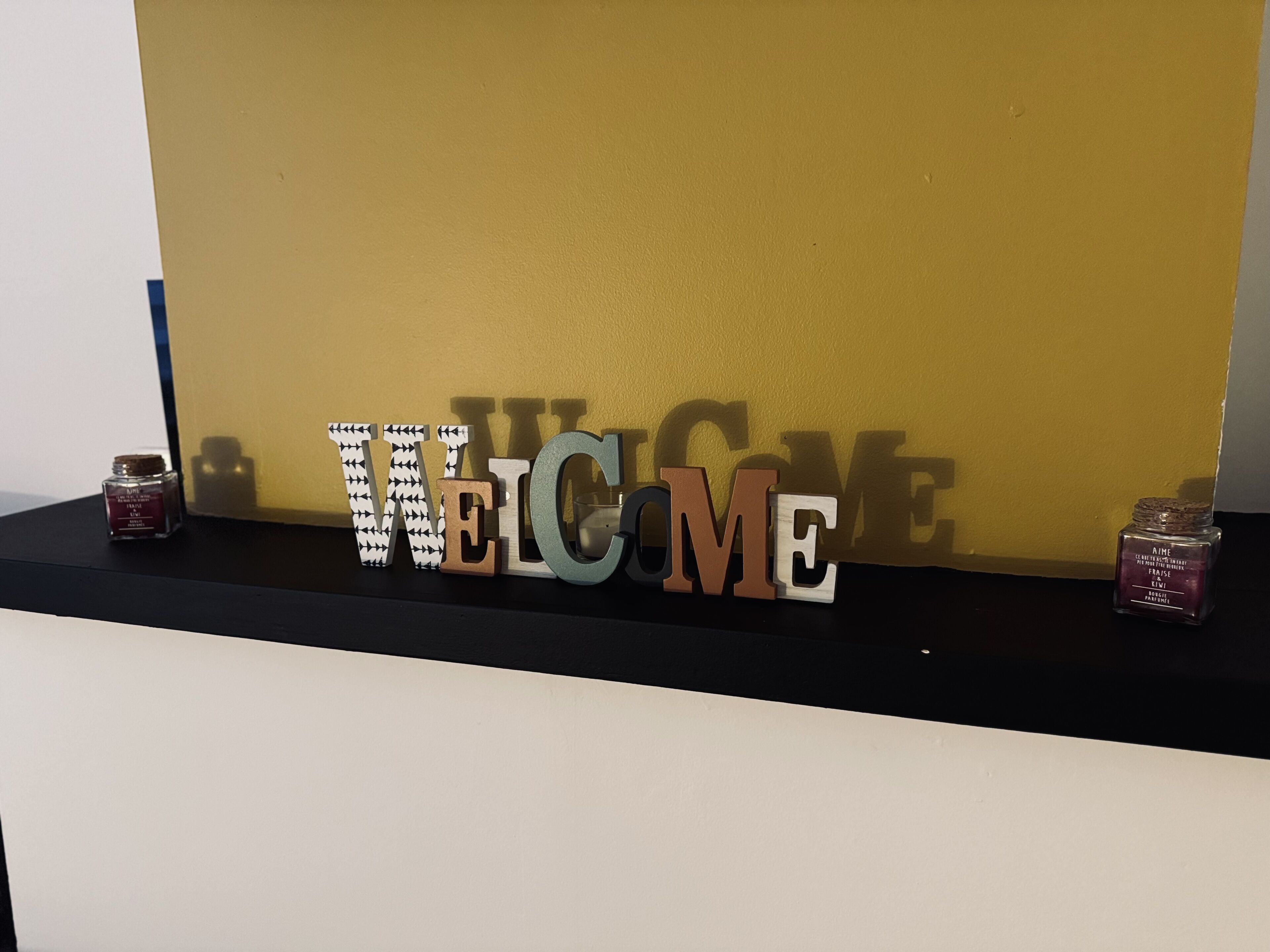 A shelf with wooden letters spelling "WELCOME" against a yellow wall.