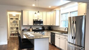 Une cuisine moderne avec des meubles blancs, des appareils en acier inoxydable, un plan de travail en granit et un îlot central doté de tabourets de bar.