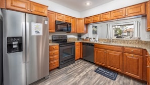A modern kitchen with wooden cabinets, stainless steel appliances, granite countertops, and a window with a view.