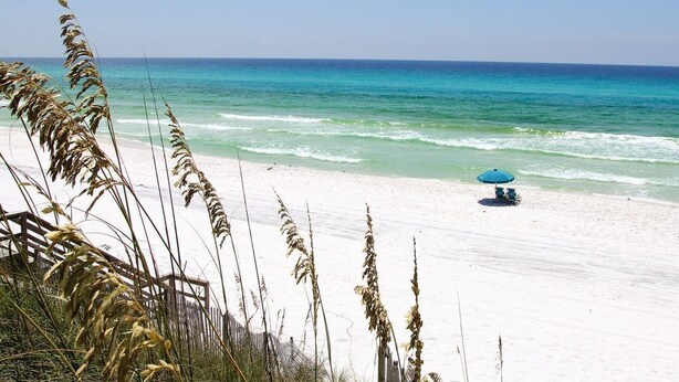 A beach with a clear view of the ocean, a sandy shore, and a blue umbrella.