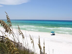 A beach with a clear view of the ocean, a sandy shore, and a blue umbrella.