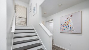 A staircase with white railings and dark steps, leading to a hallway with white walls and a wooden floor.