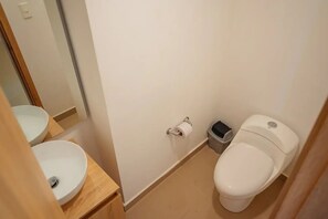 A small bathroom with a toilet, a sink, and a trash bin.