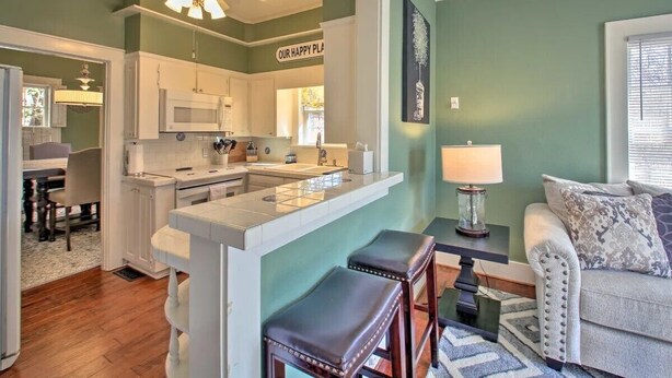 A modern kitchen with white cabinets, a central island, and a dining area with a table and chairs. - Secluded Retreat with Pool, King Beds in a Historic District, 2 mi from Oaklawn! (Hot Springs)