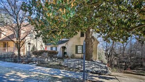 A residential property with a large tree in the foreground, a paved driveway, and a house with a sloped roof and green shutters. - Secluded Retreat with Pool, King Beds in a Historic District, 2 mi from Oaklawn! (Hot Springs)