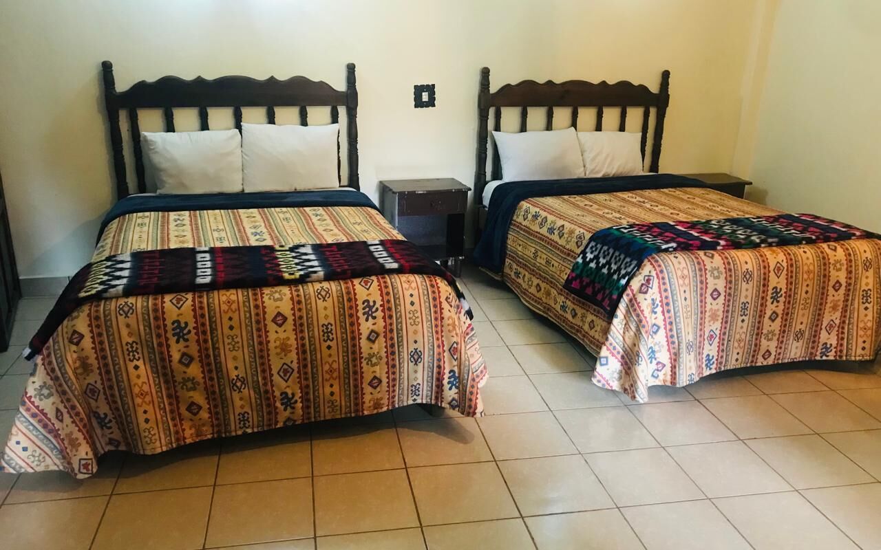 Twee eenpersoonsbedden met houten hoofdborden en bijpassende beddengoed in een kamer met betegelde vloer.