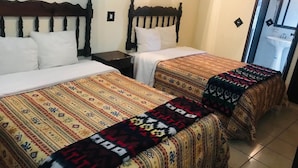 Une chambre d’hôtel avec deux lits, chacun recouvert d’une couvre-lit à motifs et agrémenté d’un plaid assorti. Il y a une petite table entre les lits et un miroir au mur.