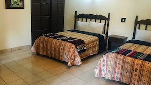 Une chambre avec deux lits, chacun agrémenté de draps à motifs, un sol carrelé, une porte en bois foncé et une petite table de chevet.