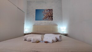 Una cama bien hecha con dos toallas y un pequeño adorno, un cabecero, lámparas de noche y un cuadro en la pared.