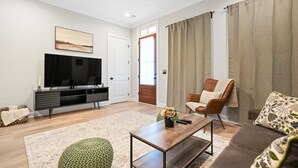 En moderne stue med et fladskærms-tv, en sofa, et sofabord og en lænestol.
