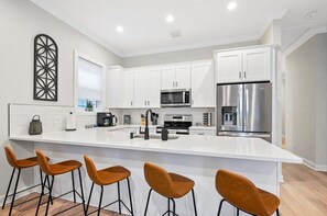 A modern kitchen with white cabinetry, stainless steel appliances, and a central island with bar stools. - Historic District Gem - 2BR/2BA, Walk to Forsyth Park - Lower Level (Savannah)