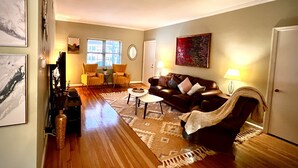 Un salon avec un canapé en cuir marron, une table basse et un tapis. On y trouve deux fauteuils jaunes, un téléviseur et des œuvres d’art accrochées aux murs.