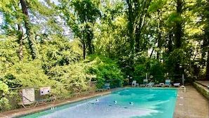 Une piscine rectangulaire à l’eau d’un bleu limpide, entourée d’une clôture en métal et d’arbres.