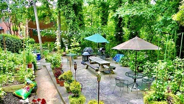 Un espace patio aménagé avec une table et des chaises, entouré de plantes en pot et d’un petit jardin.
