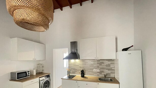 A compact kitchen with white cabinetry, a microwave, a washing machine, and a refrigerator. - Apartamento Norte (Arrecife)