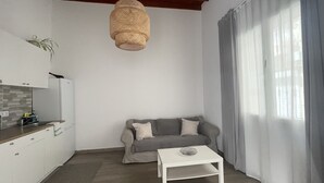 A modern living room with a grey sofa, a white coffee table, and a kitchen area with a white cabinet and a hanging plant. - Apartamento Norte (Arrecife)